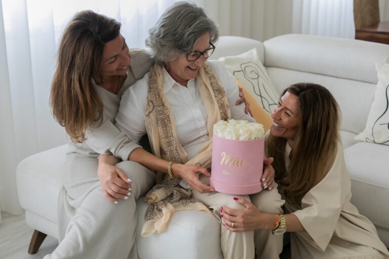 Mãe idosa sentada no sofá a receber uma caixa de flores da Flores no Cais das suas duas filhas